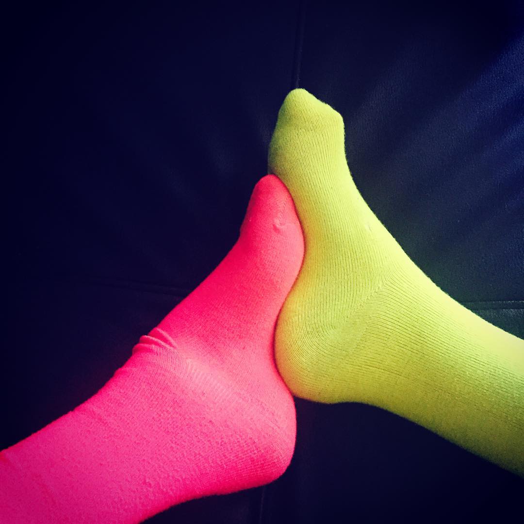 Two high arched feet in neon socks, one pink and one yellow, interlock.